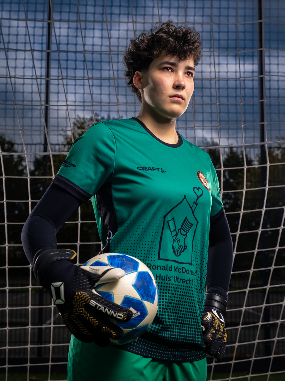 Energiek en Dynamisch PhiPho Voetbal Portret van keepster Zoe C.O.V. Desto met off-camera flash. Zoe draagt het groen-zwart keeperstenue, van sportmerk Craft en DAKA, sponsor Ronald McDonald Huis Utrecht, Stanno keepershandschoenen en heeft een Champions League bal vast. Zoe kijkt met een gefocuste blik.